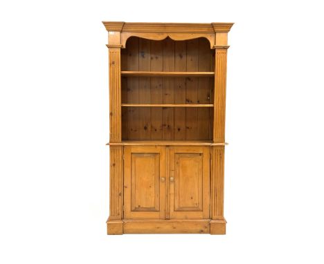 20th century varnished pine bookcase on cupboard, projecting cornice over shaped apron, two adjustable shelves flanked by flu