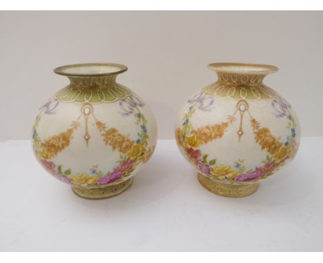 A pair of Edwardian ceramic vases of ovoid form: short flaring necks and decorated in enamels with swags of various flowers, 