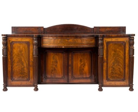 A Regency mahogany sideboard:, of bowed and breakfront outline, the ledge back with a domed arch centre and reeded mouldings,