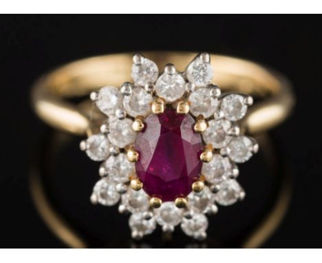 An 18ct yellow gold, ruby and diamond oval cluster ring: the oval ruby 6.8mm long x 4.9mm wide x 3.2mm deep and within a surr