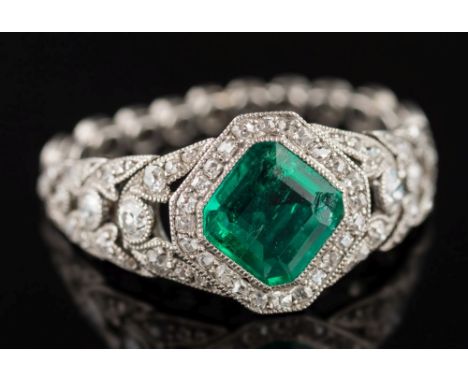 An emerald and diamond ring: the step-cut emerald approximately 7.5mm corner to corner x 2.8mm deep, within a millegrain set 