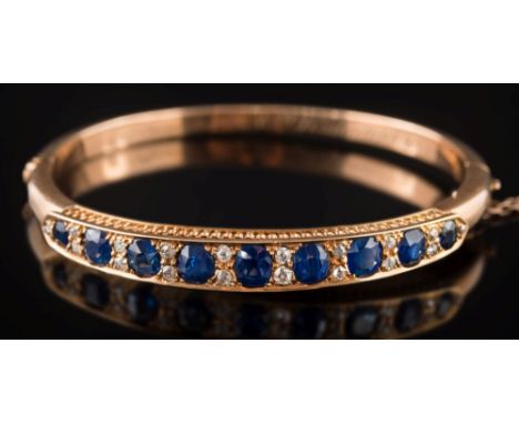A late 19th/early 20th century gold, sapphire and diamond mounted hinged bangle: with nine oval sapphires, graduated from 4.2