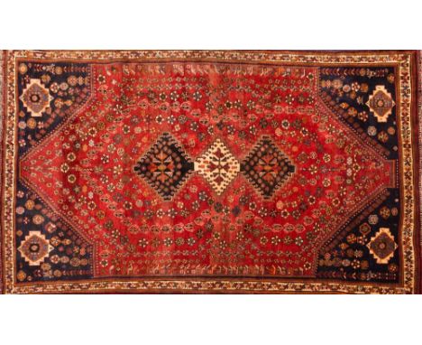 An Iranian carpet of Shiraz design:, the brick red field with triple serrated lozenge medallions and all over geometric boteh