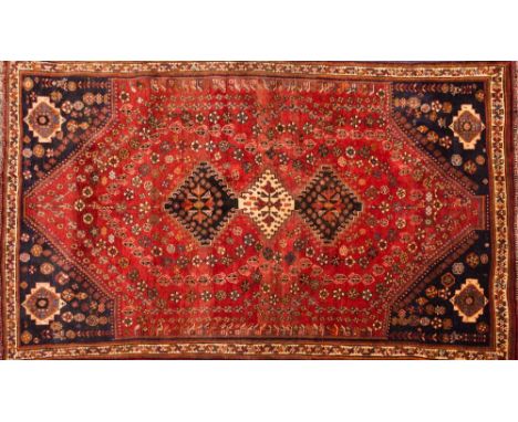 An Iranian carpet of Shiraz design:, the brick red field with triple serrated lozenge medallions and all over geometric boteh