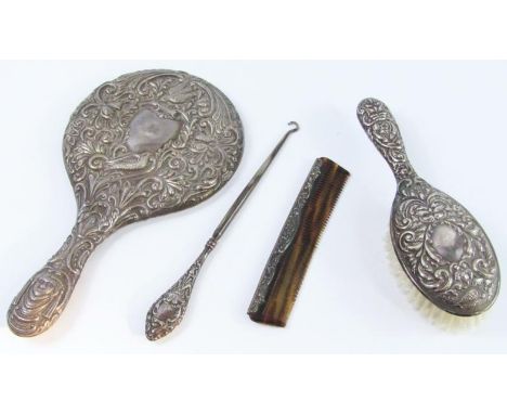 A silver backed four piece dressing table set embossed with birds, mask and foliate scrolls, comprising hair brush, hand mirr