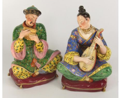 A pair of Jacob Petit porcelain scent bottles and stoppers, modelled as Turks, each seated on a cushion playing a musical  in