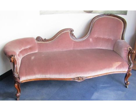 A Victorian mahogany chaise longe, with a shaped back and scroll arms, floral carving, upholstered in button back pink draylo