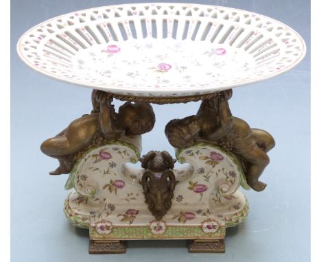 Pierced ceramic centrepiece with brass figural putti supports and masked goat decoration raised on four ornate brass feet, wi