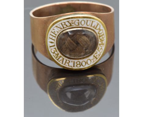 Georgian mourning ring set with plaited hair in a glass compartment surrounded by white enamel border reading "Henry Gould OB