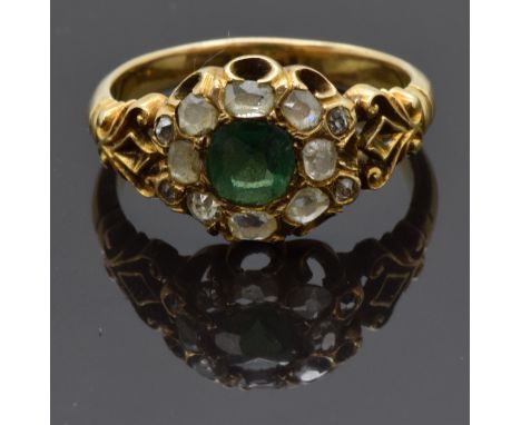 An early Victorian ring set with a cushion cut emerald of approximately 0.5ct surrounded by old cut diamonds, with scrolling 