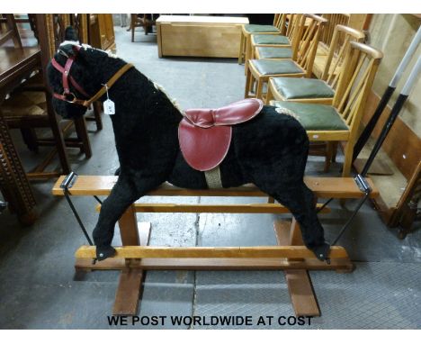 A vintage rocking horse with black coat, blonde mane and tail and red tack, on wooden base