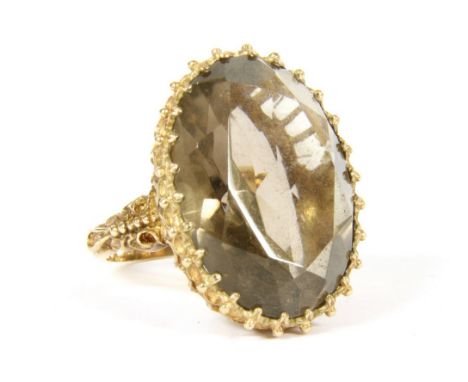 A 9ct gold single stone smokey quartz ring , claw set to an open scalloped gallery, to scrolling shoulder and a polished shan
