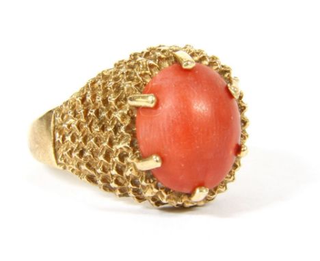 A 9ct gold single stone oval coral cabochon ring , claw set to textured fish scale heads, 5.11g