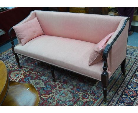 A Victorian mahogany framed faded pink linen upholstered sofa, with moulded scroll end arms and raised on three turned and fl