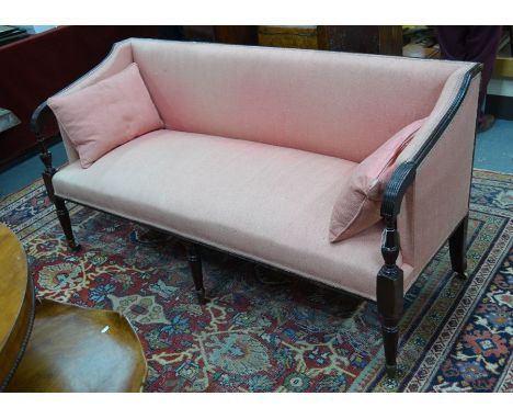 A Victorian mahogany framed faded pink linen upholstered sofa, with moulded scroll end arms and raised on three turned and fl