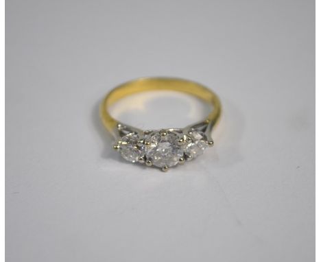 A three-stone diamond ring, the central circular brilliant cut diamond with a smaller diamond on each side, yellow metal stam