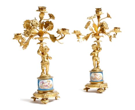 A pair of Louis XVI style ormolu figural candelabra, each modelled with a cherub holding a cornucopia of flowers and leaves, 