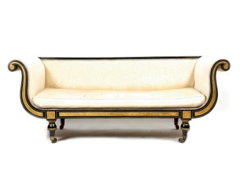 A Regency ebonised and gilt sofa, with scroll arms, upholstered in ivory watered silk with a squab cushion and on turned tape