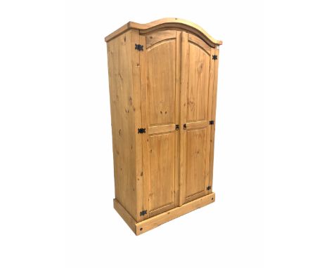 Traditional pine wardrobe, the arched top over two panelled doors enclosing interior fitted for hanging and with shelf, raise