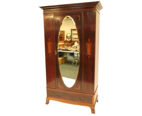 An Edwardian mahogany and inlaid wardrobe, the top with a moulded cornice above an oval bevelled mirror door, enclosing hangi