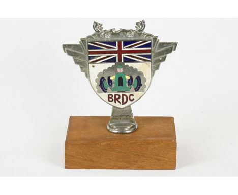 A vintage enamel car grill badge for 'BRDC' mounted to wooden plinth. 