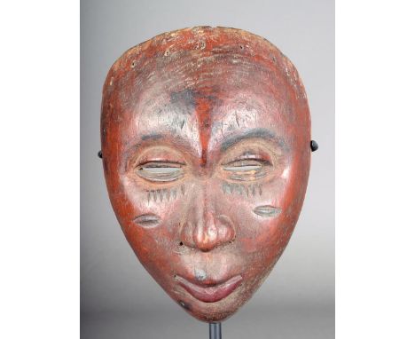 A Yoruba Egungun mask Nigeria carved wood with a red/brown finish with pierced eyes and scarifications below pierced nostrils
