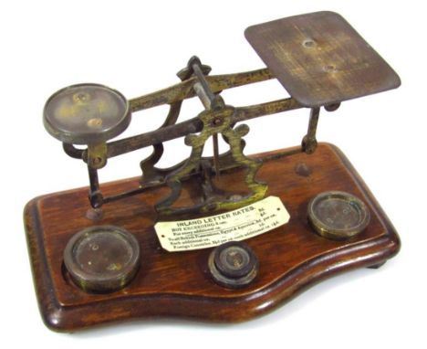 An early 20thC brass postal scale, on serpentine shaped oak stand, with a variety of weights, 21cm wide.