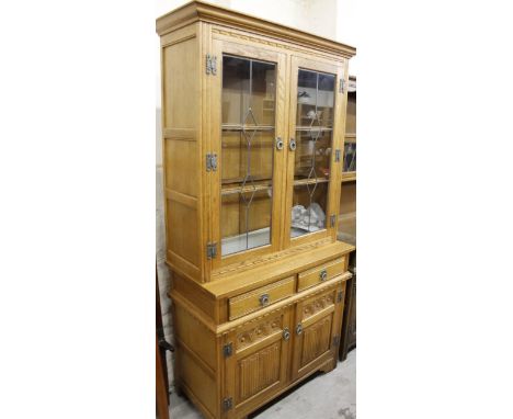 A modern light oak finish Old Charm display cabinet, the upper section with over hanging cornice raised above two lead style 