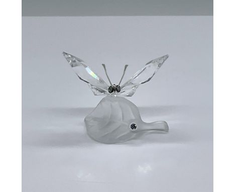 Clear faceted crystal figure of a butterfly resting on a frosted crystal leaf. It has blue/green eyes and wire antenna. Swaro