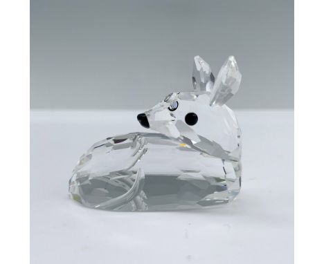 A small fawn resting on all fours, with its head turned backward to observe its surroundings, featuring striking black crysta