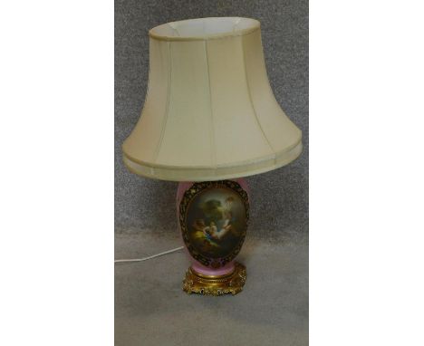 A large porcelain lamp base of bulbous form with rose pink background and hand painted cartouche depicting cherubs in a class