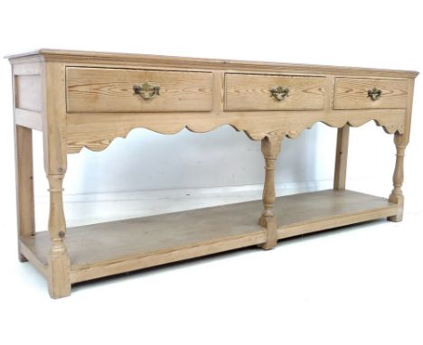 A mid 20th century pine sideboard, three frieze drawers with brass handles, shaped apron, floor level pot shelf, three turned