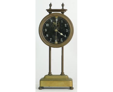 A British made brass gravity clock, the glass face with painted numerals, inside is a pendulum on a swing suspension housing 