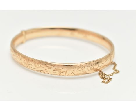 A 9CT GOLD HINGED BANGLE, with engraved scrolling acanthus decoration throughout to the hidden push piece clasp, with safety 