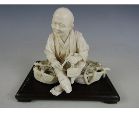 A Meiji Japanese single-piece ivory okimono carved in depiction of an elderly man, sat atop his yoke and baskets of fruit, ho