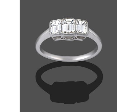 A Diamond Three Stone Ring, the graduated emerald-cut diamonds in white millegrain settings, to a tapered shoulder plain poli