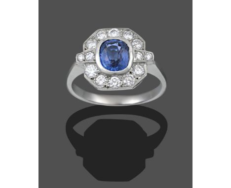 An Art Deco Style Sapphire and Diamond Cluster Ring, the cushion cut sapphire in a white millegrain setting within a border o
