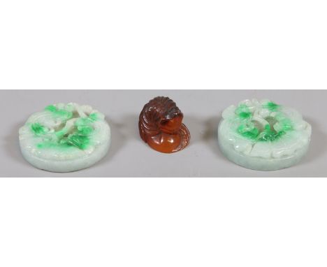 A Japanese Meiji period carved amber netsuke formed as a cat, signed along with two Chinese jadeite medallions carved with ru