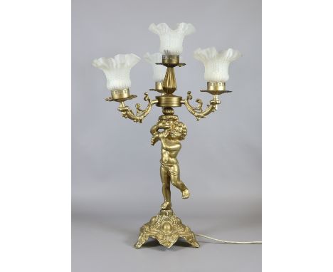 A gilt metal four branch figural lamp surmounted by a putti holding a cornucopia and with frosted glass shades.