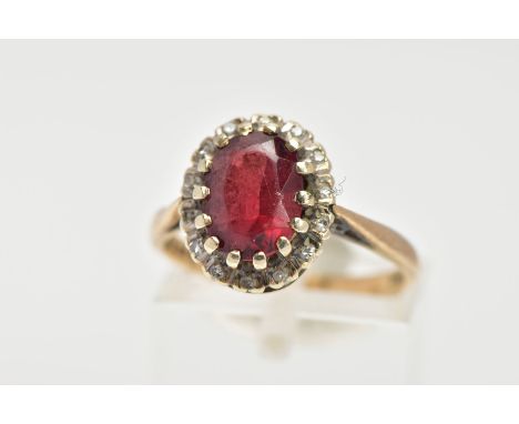 A GARNET AND DIAMOND CLUSTER RING, an oval cut almandine garnet surrounded with a halo of round brilliant cut diamonds, stone