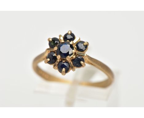 A 9CT GOLD SAPPHIRE CLUSTER RING, seven circular cut sapphires prong set in a floral design, leading onto a matt finished pin