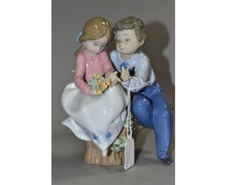 A LLADRO FIGURE GROUP 'JUST A LITTLE KISS', NO. 5701,  a boy and girl sitting on a tree stump, designed by Antonio Ramos, iss