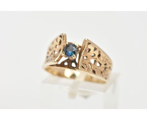 A YELLOW METAL BLUE SAPPHIRE RING, designed with a central circular cut blue sapphire, four claw setting, openwork detailed s