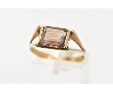 A SMOKEY QUARTZ DRESS RING, rectangular cut Smokey quartz stone, set in a yellow metal bezel setting, bifurcated  shoulders, 