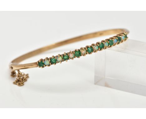 A 9CT GOLD EMERALD AND OPAL BANGLE, hinged bangle, designed with a row of circular cut emeralds interspaced with opal cabocho