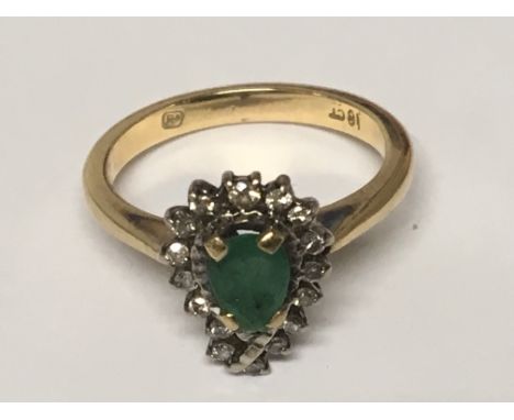 An 18ct gold ring set with an Emerald surrounded by a pattern of small diamonds.