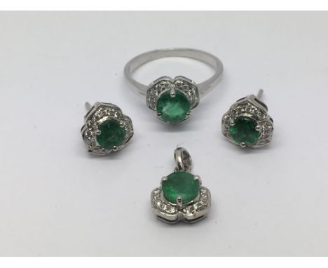 A white gold ring set with an emerald and surrounded by diamonds together with a matching pair of earrings and a pendant, rin