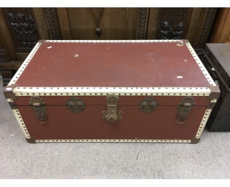 A large travelling trunk with red material covering. Measures approximately 92cm long x 50cm deep x 37cm tall.