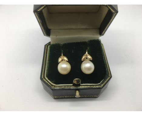 A pair of cultured pearl stud earrings decorated with leaves.