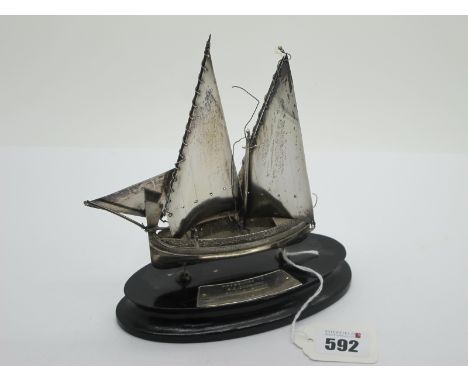 A Small Model Boat, at sail (damage) (stamped marks), on oval plinth base with applied plaque "Presented to S.E. Dods Esq. by